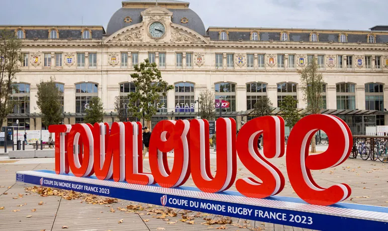 Lettrage 3D "Toulouse" en lettres rouges, sur un socle bleu sur lequel est inscrit "Coupe du Monde de Rugby France 2033". Devant le parvis de la gare Matabiau.